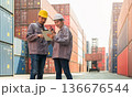 Two logistics workers in hard hats and uniforms using digital tablet and walkie talkie for loading containers control at cargo shipping container yard 136676544