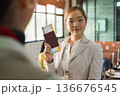 Woman at airport holding passport and boarding pass with smile while standing at check in counter 136676545