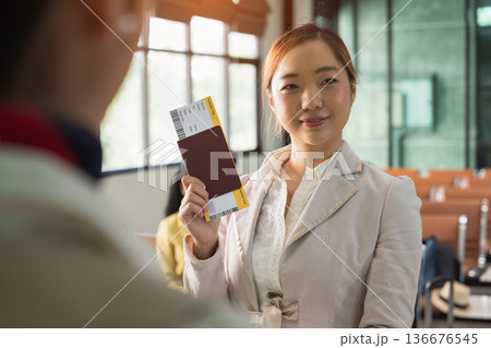 Woman at airport holding passport and boarding pass with smile while standing at check in counter Woman at airport holding passport and boarding pass with smile while standing at check in counter 136676545