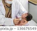 Female doctor in white coat using stethoscope to check newborn baby heartbeat while holding infant with one hand 136676549