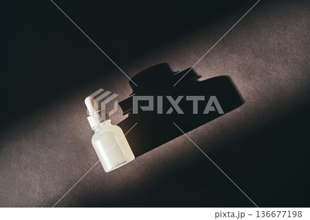 Skincare serum dropper bottle casting shadow on dark background 136677198