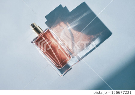 Perfume bottle creating artistic shadows and light patterns on light blue background 136677221