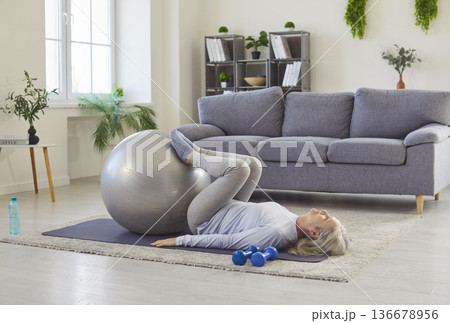 Healthy sport exercise with fitness ball of senior woman, lying on home floor with feet on ball Healthy sport exercise with fitness ball of senior woman, lying on home floor with feet on ball 136678956