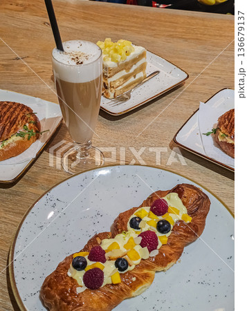 Side View of Latte Coffee with Pineapple Roll, Berry Tart and Ham Sandwich 136679137