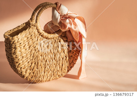 Woven Straw Handbag with Silky Scarf. Elegant Summer Fashion Flatlay on Peach Background 136679317