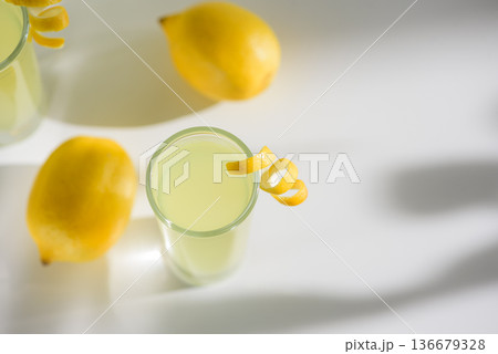 Limoncello Glasses with Curled Lemon Peels and Fresh Lemons. Refreshing Summer Italian Beverage 136679328