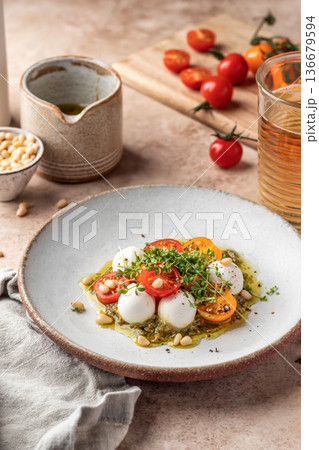 Caprese salad with fresh mozzarella balls and sliced tomatoes, served with micro greens and pesto sauce on beige background. Italian food Caprese salad with fresh mozzarella balls and sliced tomatoes, served with micro greens and pesto sauce on beige background. Italian food 136679594