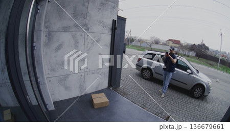 Courier in Silver Car Places Parcel on Porch and Takes Smartphone Photo For Confirmation 136679661