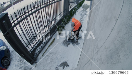Male Utility Worker Wearing Reflective Jacket Removes Snow From Paved Walkway Beside Fence Male Utility Worker Wearing Reflective Jacket Removes Snow From Paved Walkway Beside Fence 136679665