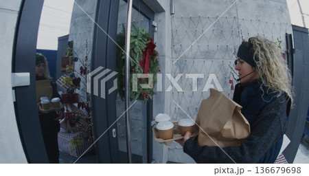 Female Courier With Headset Delivers Hot Coffee Cups and Brown Paper Bag to Man Doorstep 136679698