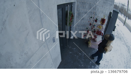 Female Passerby Approaches Festively Decorated House, Notices Parcel on Porch, Quickly Picks it Up Female Passerby Approaches Festively Decorated House, Notices Parcel on Porch, Quickly Picks it Up 136679706
