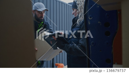 Man Moves Parcels From Pallet Jack Into Blue Van While Woman Scans Barcodes and Checks Tablet 136679737