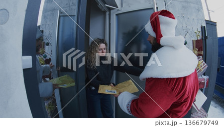 Postal Courier Dressed in Santa Costume Delivers Envelope Woman at Doorstep Postal Courier Dressed in Santa Costume Delivers Envelope Woman at Doorstep 136679749