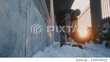 Focused Man Uses Plastic Shovel For Manual Property Upkeep Near Wall and Metal Fence 136679859