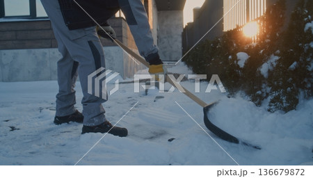 Adult Male Laborer Performs Physical Labor By Lifting and Throwing Snow With Shovel Near Building Adult Male Laborer Performs Physical Labor By Lifting and Throwing Snow With Shovel Near Building 136679872
