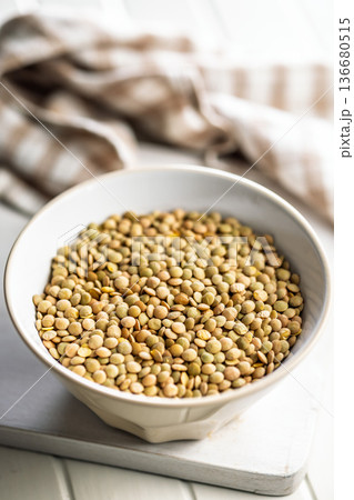 Uncooked green lentil in bowl on white table. Uncooked green lentil in bowl on white table. 136680515