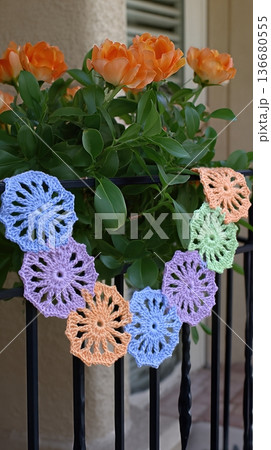 Crochet Garland Displays Colorful Flowers Near Blooming Roses on a Sunny Day Outdoors 136680555
