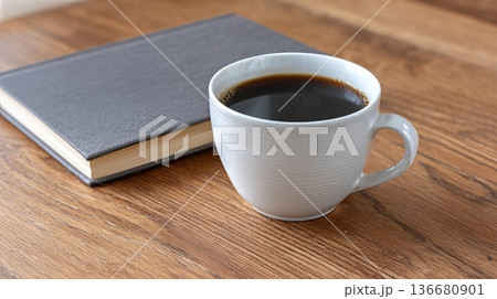 Coffee Cup Sits Next to a Closed Notebook on a Wooden Table During a Quiet Morning Coffee Cup Sits Next to a Closed Notebook on a Wooden Table During a Quiet Morning 136680901