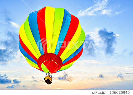 Colorful hot air balloon flying under orange sunset sky 136680940