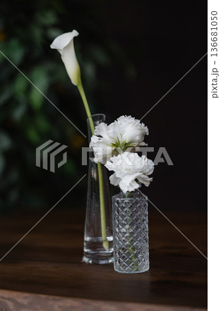 White calla lily in tall vase with small carnations on wooden table against green background 136681050