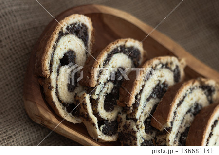 Rustic presentation of sliced poppy seed roll on a wooden serving board with burlap cloth underneath Rustic presentation of sliced poppy seed roll on a wooden serving board with burlap cloth underneath 136681131