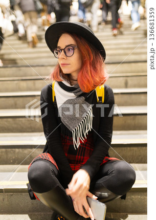 Young woman sitting on stairs watching bustling city life Young woman sitting on stairs watching bustling city life 136681359