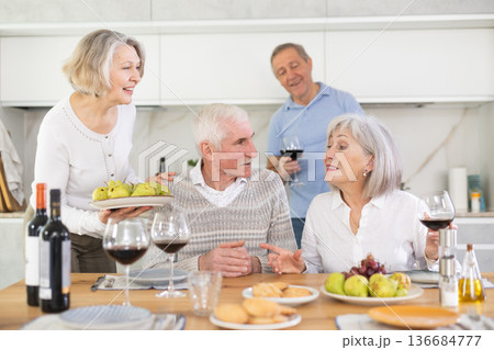 During feast, elderly housewife sets table, puts on desk snack for wine, large platter with fruits During feast, elderly housewife sets table, puts on desk snack for wine, large platter with fruits 136684777