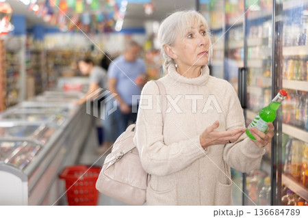 Old woman purchaser choosing cool drink in big supermarket 136684789