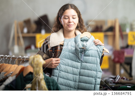 Young girl choosing light green vest for autumn-winter in clothing store 136684791