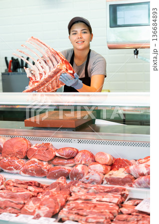 Sales assistant girl shows beef flat ribs in butcher shop Sales assistant girl shows beef flat ribs in butcher shop 136684893
