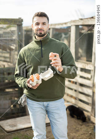 Positive man stands and holds in hands palms few fresh chicken eggs 136684945