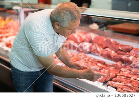 Adult man buyer chooses beef in butcher shop Adult man buyer chooses beef in butcher shop 136685027