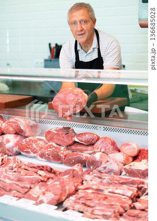 Adult man seller lays out beef in butcher shop Adult man seller lays out beef in butcher shop 136685028