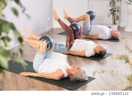 People lying on karemat, pulled bent legs to themselves and clamped soft-ball in knee 136685122