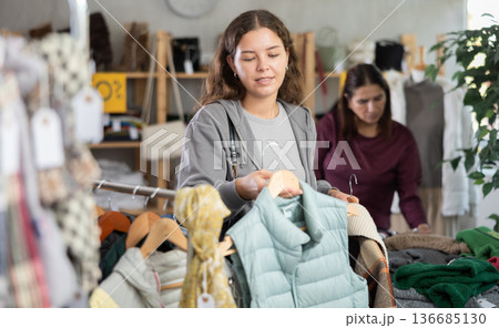 Young girl choosing light green vest for autumn-winter in clothing store Young girl choosing light green vest for autumn-winter in clothing store 136685130
