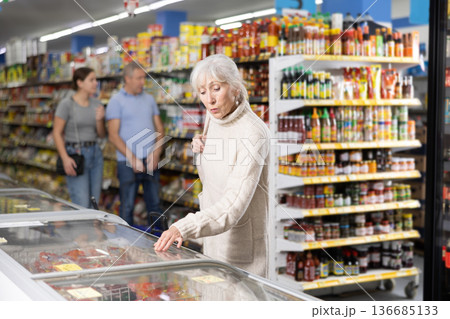 Elderly woman looking at products in glass refrigerator in food store 136685133