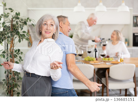 Senior man and woman doing couple dancing with their backs to each other during house party. 136685151