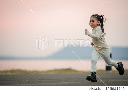 little child girl running happily on an open road by the water at sunset 136685443