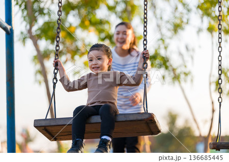 cheerful child girl with mother playing on swing at playground cheerful child girl with mother playing on swing at playground 136685445