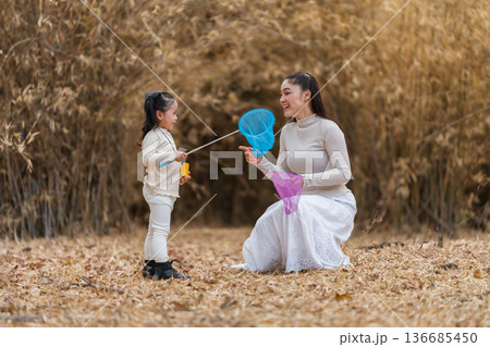Mother and child girl bonding while playing with butterfly nets in dry forest. Mother and child girl bonding while playing with butterfly nets in dry forest. 136685450