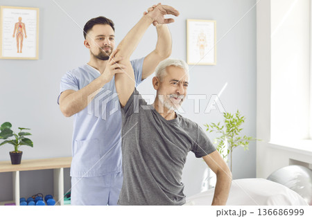 A rehabilitation therapist helps an elderly man raise his arm, close-up A rehabilitation therapist helps an elderly man raise his arm, close-up 136686999