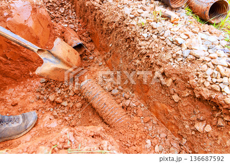 Construction crew digs trench for drainage pipe installation near residential area Construction crew digs trench for drainage pipe installation near residential area 136687592