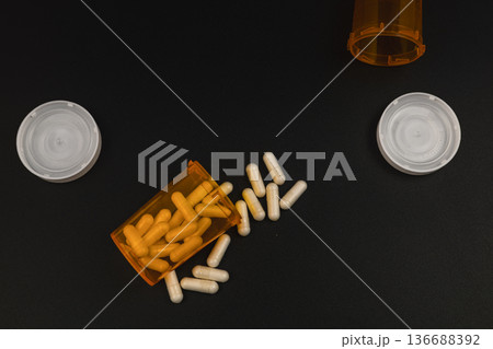 Pill bottles on a black surface with spilled capsules scattered around 136688392