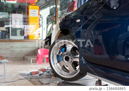 Close up of car wheel and fender repair in auto garage mechanic working with tools on workshop floor automotive maintenance and customization process detail 136688865