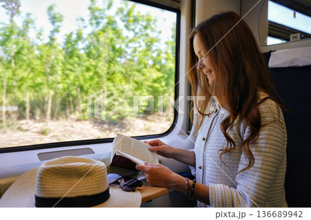 Young woman reading book on train by window during summer trip 136689942