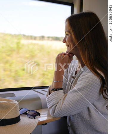 Woman looking out train window during summer journey 136689945