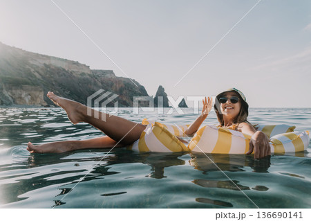 Woman, Inflatable Raft, Ocean - Woman relaxing on inflatable raft in ocean near rocky coastline. 136690141