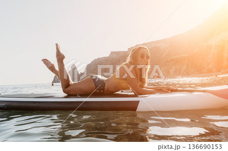 Woman Paddleboard Beach Relaxing - Young woman laying on a paddleboard in the ocean, relaxing and enjoying the summer day. 136690153