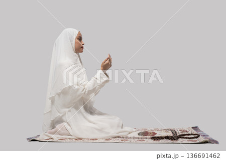 Serene woman kneeling with ritual. Woman in white headscarf performing silent ritual indoors 136691462