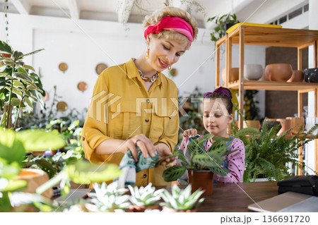 A mother and daughter enjoy tending to plants together in a bright, inviting space 136691720